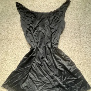 Svart satinklänning med spetsdetaljer - Vintage svart satinklänning med snygg spets längs urringningen och axlarna. Går jättebra att använda som både klänning och nattlinne! Lite stor i storleken så skulle nog passa L också😊Skriv vid frågor eller för att diskutera pris!