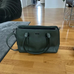 Mörkgrön axelväska  - Snygg mörkgrön axelväska från Don Donna i skinnimitation. Väskan har både handtag och justerbar axelrem samt flera fack. Dator och skolböcker får plats!!