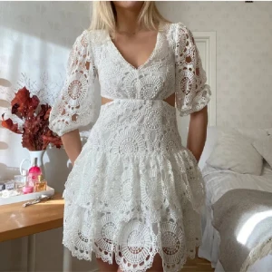 Vit spetsklänning med volang - Superfin vit kortklänning i spets med v-ringning, volangkjol och trekvartsärmar. Klänningen har snygga cut-outs i midjan och ett detaljerat broderat mönster som ger en romantisk vibe. Perfekt för sommarens alla tillfällen!