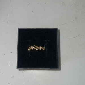 Guldig blixtformad ring med stenar - Cool ring i guldton med blixtformad design och små glittrande stenar på. Aldrig använd, tror den är rostfri😊😊 går att justera storleken lite
