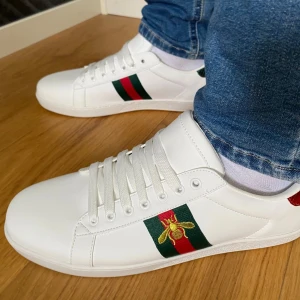 Gucci ace vita  - Säljer ett par helt nya Gucci Ace vita sneakers i storlek 43. 	                                                                          •	Oanvända och i nyskick 	                                               •	Påse, box och extra skosnören ingår                 Väldigt populära och efterfrågade skor från Gucci.   OBS!!! Inte helt säker på äktheten (därav priset).      Det är bara att skriva vid funderingar eller om du vill ha fler bilder.