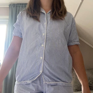 Blåvitrandiga pyjamasset  - Säljer ett par blåvitrandiga pyjamasshorts med elastisk midja och vita kantdetaljer. Shortsen är i mjuk bomull och har en klassisk, avslappnad passform. Perfekta för sommarkvällar eller mysiga morgnar hemma.