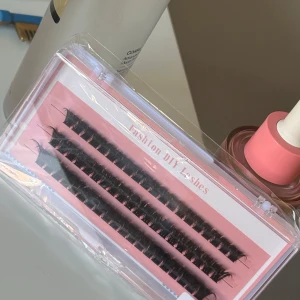 Fashion DIY Lashes fransar - Säljer ett set med svarta individuella lösögonfransar i en rosa och transparent ask. Fransarna är täta och böjda för en fyllig look, perfekta för att skapa din egen lash extension-stil hemma. Superenkla att applicera och anpassa efter önskad volym.