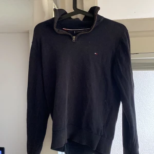 Mörkblå half zip tröja Tommy Hilfiger - Mörkblå långärmad tröja från Tommy Hilfiger i premium bomull. Klassisk modell med half zip-dragkedja i halsen och liten broderad logga på bröstet. Perfekt för dig som gillar stilrena och tidlösa plagg med en sportig touch.