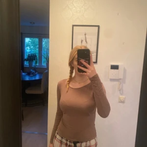 Brun långärmad topp med rund hals - Säljer en enkel brun långärmad topp med rundad halsringning. Modellen är slim och sitter snyggt mot kroppen. Materialet känns mjukt och lätt, perfekt att styla med jeans eller kjol. Passar dig som gillar basic och neutrala färger.