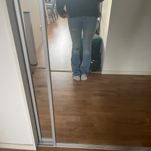 Ljusblå bootcut jeans med slitningar - Säljer ett par ljusblå jeans med bootcut-modell och snygga slitningar på låren och knäna. Jeansen har klassisk femficksdesign och är tillverkade i denim. Perfekta för dig som gillar en avslappnad och trendig look.