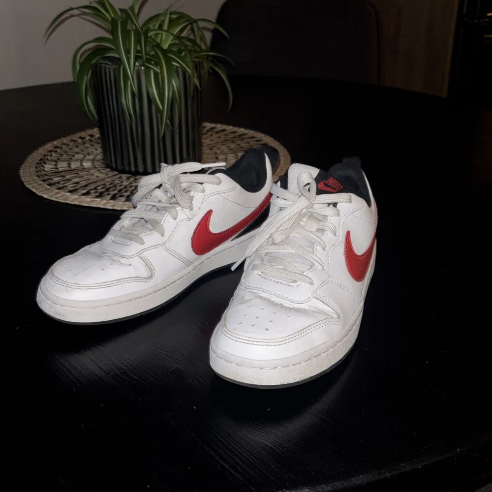 Snygga vita Nike sneakers med röda detaljer och svart insida. Skorna har klassisk snörning och en stilren design som passar perfekt för vardagsbruk. Bra skick. Box ingår. Kengät.