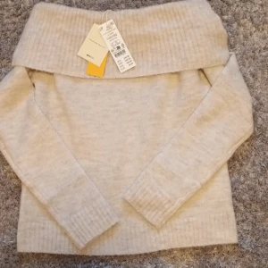 Beige off shoulder tröja från Gina Tricot - Säljer en stilren beige off shoulder tröja från Gina Tricot. Tröjan har en  ribbad kant vid axlarna och långa ärmar. Perfekt för en avslappnad och trendig look. Helt ny med prislapp.