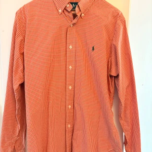 Orange rutig skjorta från Ralph Lauren - Snygg orange rutig skjorta från Ralph Lauren med klassisk passform. Skjortan har långa ärmar och knappar framtill samt en broderad logga på bröstet. Perfekt för en stilren look!