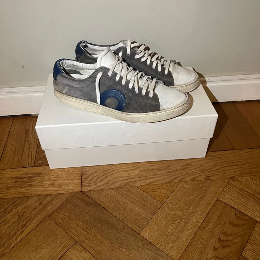 Säljer ett par grå sneakers från Oliver Cabell i modellen Low 1. Skorna har en stilren design med blå detaljer. Skick 6/10 två defekter som syns på sista bilden ! Annars är dom i 8/10. Hålet i sulan märks ingenting när du har på dig skorna !! Står ej för PostNords eller instabox strul. Hör av dig vid minsta fundering och kan absolut gå ner i pris vid snabb affär!. Kengät.