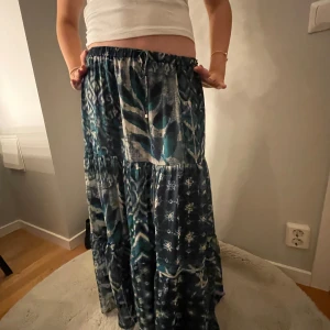 Mönstrad långkjol i blå och grön - Säljer en bohemisk långkjol med ett unikt mönster i blå och gröna toner. Kjolen har en avslappnad passform och är perfekt för en stilfull look. Den har ett elastiskt midjeband för extra komfort.