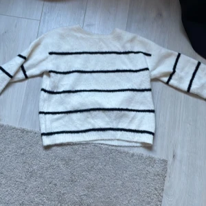 Vit och svart randig tröja från Kappahl - Säljer en mysig vit tröja från Kappahl med svarta ränder. Tröjan har en rund hals och långa ärmar, perfekt för kyligare dagar. Den är gjord i ett mjukt material som känns skönt mot huden.🖤🤍