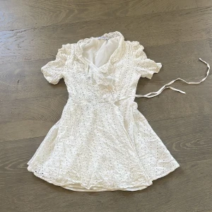 Vit spetsklänning med knytband - Charmig vit klänning i spets med korta ärmar och knytband i midjan. Klänningen har en omlott-design och v-ringad hals, perfekt för sommarens festligheter. Perfekt till studenten❤️ Obs väldigt kort så man måste vara max 1.60 lång annars funkar det med korta vita shorts under😁