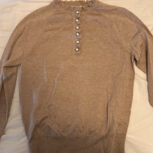 Beige/brun classy tröja  - Beige tröja från Holly & Whyte by Lindex. Tröjan har långa ärmar och dekorativa pärlknappar framtill. Den har en ribbad krage och muddar.
