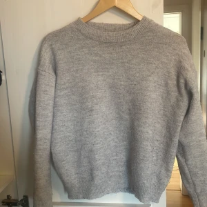Grå stickad tröja från Gina Tricot - Säljer en mysig grå stickad tröja från Gina Tricot. Tröjan har en rund halsringning och långa ärmar med ribbade muddar. Perfekt för kyliga dagar! 