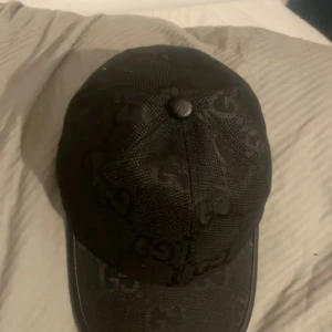 Svart keps från Gucci - Snygg svart keps från Gucci med det ikoniska GG-mönstret. Kepsen har en justerbar rem baktill för perfekt passform. Tillverkad i Italien med högkvalitativa material.
