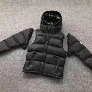 Svart dunväst från Burberry - Snygg svart dunväst från Burberry med avtagbara ärmar och huva. Västen har en quiltad design och stängs med dragkedja och knappar. Insidan har ett klassiskt rutigt mönster. Perfekt för kyliga dagar!