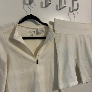 Tränings set - Ett vit-beiget träningsset med en långärmad zip tröja och ett par shorts i lår längd.