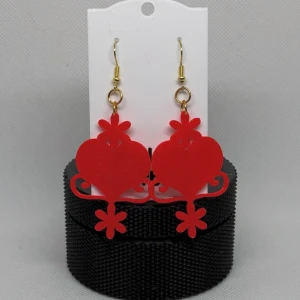 Röda hjärtformade örhängen kurbits Dalarna  - Snygga röda örhängen i hjärtform med dekorativa detaljer. Egen design med inspiration av kurbits. De har en glittrig yta och hängs upp med guldfärgade krokar. Perfekta för att ge en färgklick till din outfit.