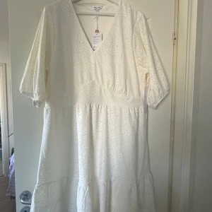 Vit klänning med spetsdetaljer - Charmig vit klänning med v-ringning och spetsdetaljer. Klänningen har trekvartsärmar och en luftig passform, perfekt för varma dagar. Den har en romantisk känsla med sitt fina mönster och mjuka material.