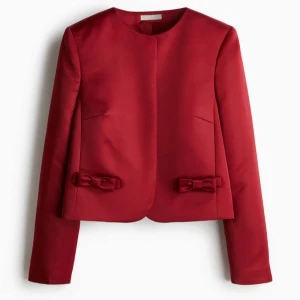 Röd kavaj - Elegant röd kavaj i satin från h&m storlek xs, med rund hals och dekorativa rosetter framtill. Perfekt för en stilren look. Slutsåld, använd 1 gång