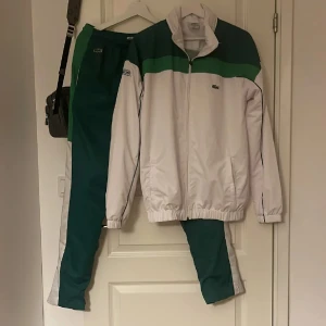  Lacoste tracksuits  - BEHÖVER PENGAR AKUT!!Säljer en stilren vit och grön träningsdräkt från Lacoste. Säljer den åt min vän han sa att fick den av sin kusin. Jackan har dragkedja och elastiska muddar, medan byxorna har en bekväm resår i midjan. Perfekt för sportiga aktiviteter eller en avslappnad stil.