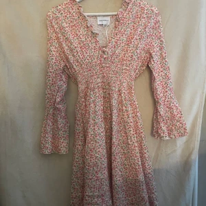 Blommig klänning från American Dreams - Säljer en söt blommig klänning från American Dreams i rosa och grönt. Klänningen har långa ärmar med volangdetaljer och en smickrande v-ringning. Perfekt för vår och sommar!