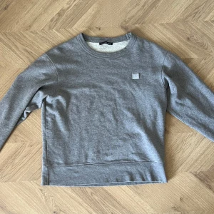 Grå sweatshirt från Acne Studios - Säljer en stilren grå sweatshirt från Acne Studios. Tröjan har en rund halsringning och en diskret logotyp på bröstet. Perfekt för en avslappnad look.