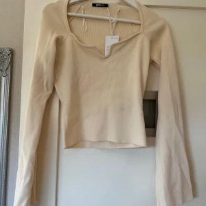 Beige ribbad topp från Gina Tricot - Säljer en stilren beige ribbad topp från Gina Tricot. Toppen har en v-ringad design och långa ärmar, perfekt för en chic och avslappnad look. Passar bra till både jeans och kjol. Perfekt för vårens garderob! Helt ny med prislapp