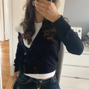 Svart kofta med knappar - Säljer en stilren svart kofta med knappar framtill. Perfekt för lager-på-lager och passar till många olika outfits. Koftan har långa ärmar och en klassisk rund halsringning. Dem 2 första bilderna är mina egna, den sista är tagen ur hm hemsida! Storlek M men passar mig som oftast bär S. Pris kan diskuteras 