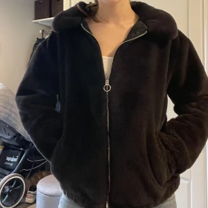 Svart teddyjacka från Hollister - Mysig svart teddyjacka från Hollister med dragkedja framtill. Jackan har en fluffig textur och långa ärmar, perfekt för kyligare dagar. Den har en klassisk krage och två fickor på sidorna. Storlek i M.