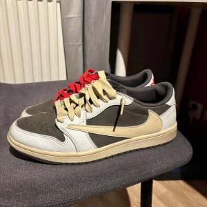 Nike Air Jordans Travis Scott - Snygga Nike Air Jordans i en stilren kombination av vitt, brunt och beige. Skorna har en unik design med kontrasterande snörning i rött och beige. Perfekta för dig som vill ha en sportig och trendig look. ❗️Ingen box eller extra skosnören❗️