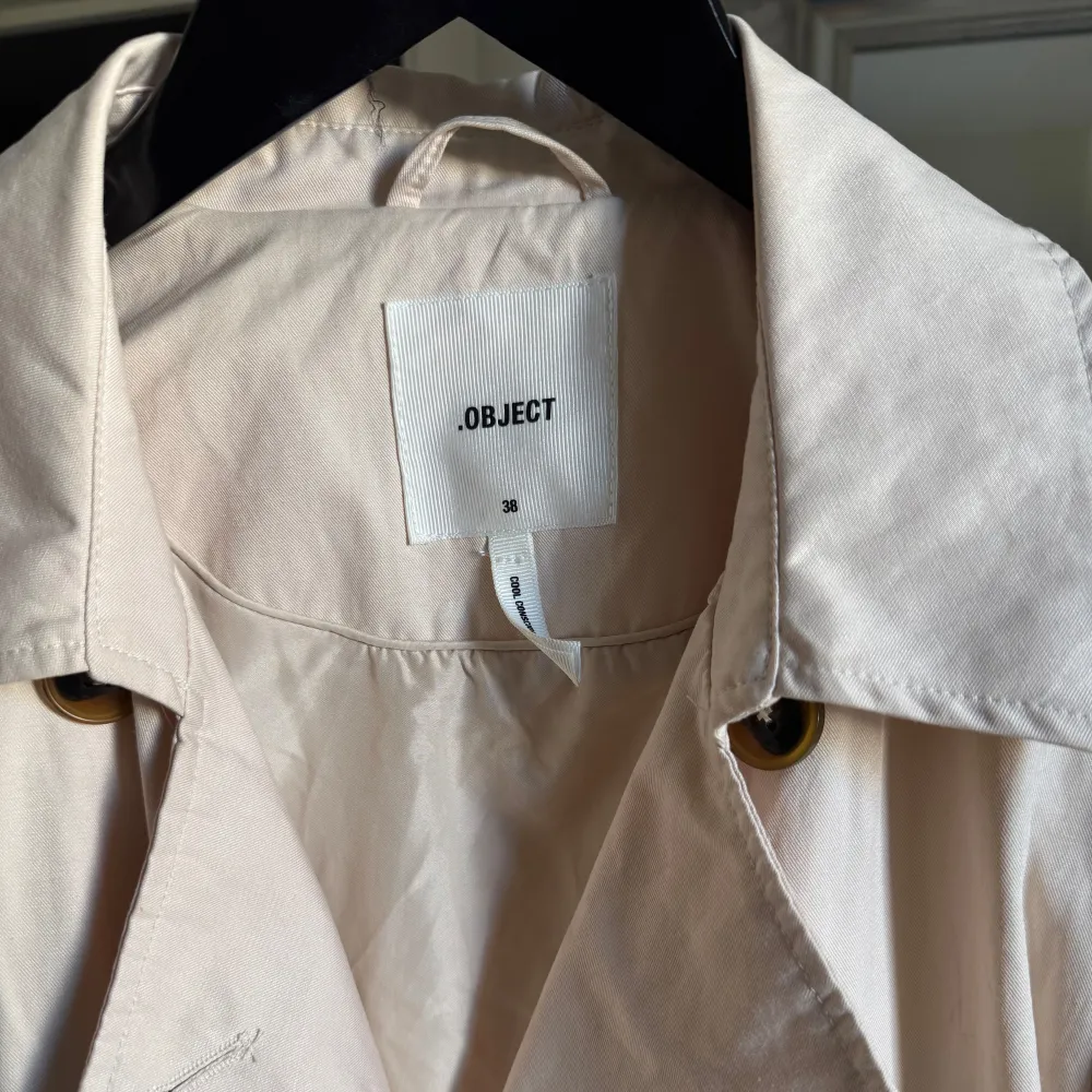 Snygg beige trenchcoat från Object med knappar och bälte i midjan. Jackan har en klassisk design med långa ärmar och en stilren look.. Takit.