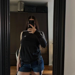 T-shirt - Snygg svart långärmad tröja från Adidas med klassiska vita ränder längs ärmarna och en vit krage. Perfekt för en sportig look eller avslappnad stil. Adidas-loggan är diskret placerad på bröstet.🥰🥰🥰