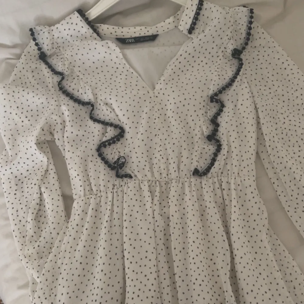 Säljer en söt vit klänning från Zara med små svarta prickar och volangdetaljer. Klänningen har långa ärmar och en v-ringad design. Perfekt för en somrig look!. Mekot.