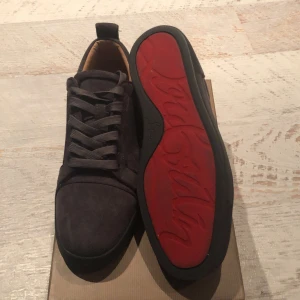 Svarta sneakers från Christian Louboutin - Snygga svarta sneakers från Christian Louboutin med en röd sula och snörning. Skorna har en stilren design med en touch av lyx. Perfekta för dig som vill ha något unikt och trendigt. 