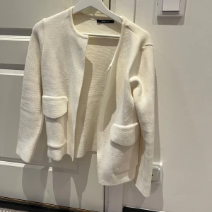 Vit cardigan jacka från Gina Tricot - Säljer en stilren vit cardigan jacka från Gina Tricot. Jackan har en öppen design med två praktiska fickor framtill. Den är långärmad och tillverkad i ett mjukt material som ger en bekväm passform. Perfekt för lager-på-lager-stil!