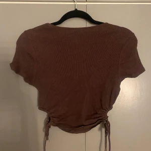 Brun ribbad topp från Divided - Säljer en brun ribbad topp från Divided. Toppen har korta ärmar och en snygg knytning i midjan som ger en fin passform. Perfekt för en avslappnad stil.
