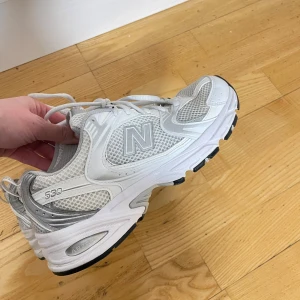 Vita sneakers från New Balance - Säljer ett par vita New Balance sneakers med grå detaljer. Skorna är varsamt använda och inga fel såsom hål eller likande. 
