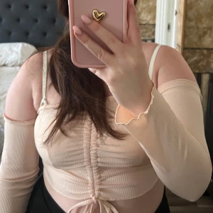 Beige ribbad offshoulder topp - Säljer en snygg beige ribbad offshoulder topp med långa ärmar och knytning framtill. Perfekt för en trendig look.