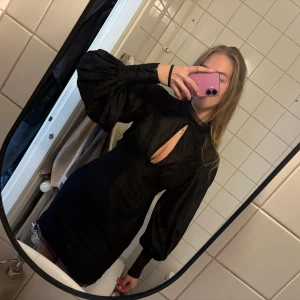 Svart klänning med spetsdetaljer - Elegant svart klänning med långa ärmar och spetsdetaljer. Klänningen har en hög hals och en liten öppning framtill. En perfekt klänning till middag eller utgång. Har endast använt den 1 gång❤️