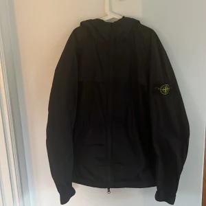 Svart jacka/windbreaker från Stone Island - Säljer en svart jacka/windbreaker från Stone Island med dragkedja och huva. Jackan är köpt på nk och är knappt använd. Perfekt till våren eller än sommar kväll. Skick 9,5 av 10. Hör av er vid funderingar👏