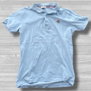 Moncler piké - Snygg ljusblå pikétröja från Moncler med klassisk krage och knappslå. Tröjan har en broderad logotyp på bröstet och är perfekt för en stilren look. Tillverkad i mjukt material för extra komfort.