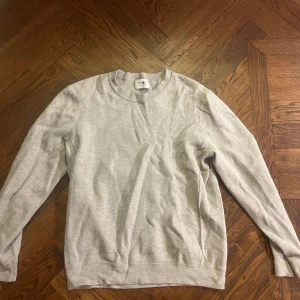 Grå tröja från NN07 - Säljer en stilren grå tröja från NN07. Tröjan har en klassisk design med rund hals och långa ärmar. Perfekt för en avslappnad och bekväm stil.