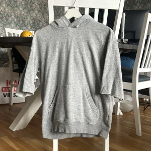 Grå hoodie från H&M - Säljer en grå hoodie från H&M Basics med korta ärmar och en praktisk magficka. Perfekt för en avslappnad stil. Hoodien har en mjuk och bekväm passform.