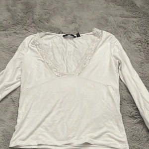 Vit långärmad spets topp från Vero Moda - Säljer en stilren vit långärmad topp från Vero Moda med v-ringning och spetsdetaljer runt halsen. Perfekt för en elegant och avslappnad look. Passar bra till både jeans och kjol. 🌟