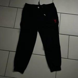 Svarta mjukisbyxor från Ami - Snygga svarta mjukisbyxor från Ami med en röd broderad logga på benet. Byxorna har en snörning i midjan för justerbar passform och är perfekta för en avslappnad stil.