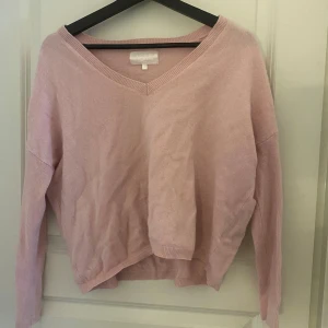 Rosa kashmirtröja från Les tricots de Léa - Säljer en mjuk och rosa kashmirtröja från Les tricots de Léa. Tröjan har en v-ringad design och långa ärmar, perfekt för en stilren och bekväm look. Passar utmärkt för kyligare dagar.