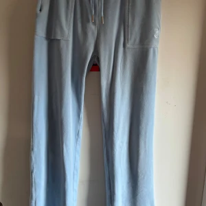 Ljusblåa  juicy Couture byxor  - Säljer ett par ljusblå mjukisbyxor med snörning i midjan och fickor med knappar. Perfekta för en avslappnad stil. Byxorna har en mjuk och bekväm känsla.säljer då de är för små 💗