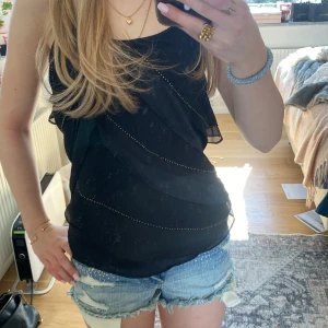 Svart ärmlös topp från Zara Basic - Snygg svart ärmlös topp från Zara Basic med volangdetaljer och tunna axelband. Perfekt för en stilren look. Toppen har en luftig passform och är tillverkad i ett lätt material.